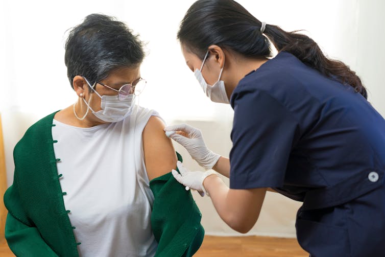 A woman receives a vaccination from a female nurse.